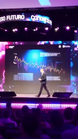 A man in a dark suit walks across a stage during a presentation. The stage is decorated with purple lights, and behind him is a large screen displaying a graph. The screen reads "THE FINGERPRINT OF THE POTENTIAL OF GENE OCEAN REGULATION". The audience is visible in the foreground, watching the presentation. Above the screen, a sign reads "CONGRESO FUTURO" or "FUTURE CONGRESS".