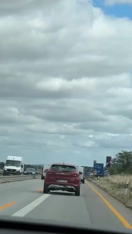 The video is a first-person perspective of driving on a highway with moderate traffic under a cloudy sky. A red Hyundai SUV is in front, followed by a white van. Road signs are visible on the right side of the highway, indicating directions and distances. The signs show "Uhyst a.t. Kamenz" and "100 m". The camera appears to be mounted inside a vehicle.
