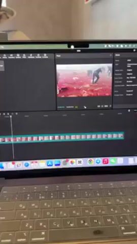The video shows a laptop screen running video editing software. The timeline at the bottom displays numerous clips, while the preview window shows a scene of multiple people in an open area covered with red material. The scene transitions to a burst of fireworks with red debris and smoke filling the area. The video continues alternating between scenes of people moving through a red-covered area and fireworks exploding. The person speaking in the video says they are editing a video for their channel.