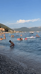 Crowded beach and cruise ship along a hilly coastline