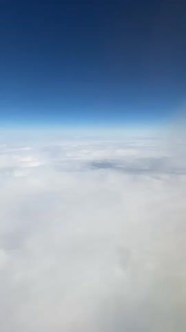 The video shows a view from above a thick layer of white clouds, under a clear, deep blue sky. The horizon line is clearly visible, separating the two layers. There are no people or other objects visible.