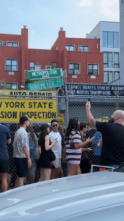 Crowd clusters behind chain-link fence near New York inspection site