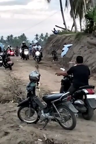 Motorcycles and crowds gather along riverbank in Kapa, Indonesia