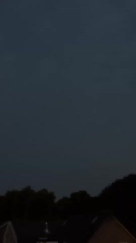 A dark sky hovers over silhouetted trees and the roofs of houses.