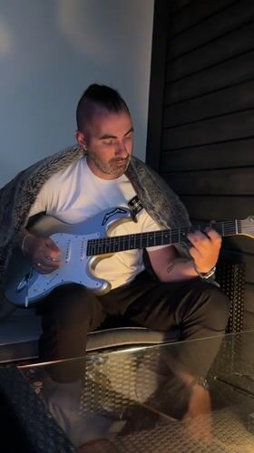 Man with mohawk plays guitar alongside Pomeranian in Oslo home