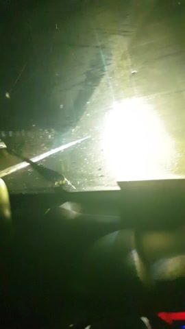 This media file provides a first-person perspective of driving at night during what appears to be heavy rain. The initial frames show raindrops on a windshield, with bright headlights from an oncoming vehicle illuminating the scene. The wipers are likely engaged, as evidenced by streaks on the glass.

As the video progresses, the view shifts to the road ahead. The road is dark and wet, reflecting the headlights of the vehicle and distant lights. There are indications of vegetation and possibly a fence or barrier along the side of the road. In some frames, there appears to be standing water on the road, suggesting a flooded or poorly drained area. The overall impression is that of a challenging drive through adverse weather conditions in a rural or semi-rural setting in Paramankeni, India, at nighttime. The emotions conveyed are primarily those of focus and caution, necessary for navigating in such conditions. No discernible text is visible in the video.