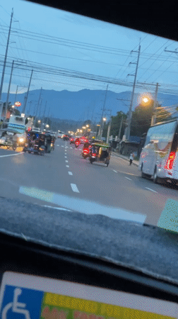 Car travels past tricycles on mountain-view road in Davao