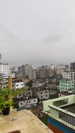 Rainy rooftop morning in Dhaka with a school worksheet in hand