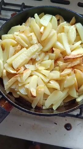 THE VIDEO SHOWS A CLOSEUP SHOT OF POTATOES BEING FRIED IN A PAN ON A STOVE. THE POTATOES ARE CUT INTO WEDGES AND ARE GOLDEN BROWN AND CRISPY. THE PAN IS BLACK CAST IRON AND IS SITTING ON A WHITE STOVETOP. THE BACKGROUND IS BLURRY BUT APPEARS TO BE A KITCHEN SETTING. THERE ARE NO PEOPLE VISIBLE IN THE VIDEO. THE VIDEO IS VERY SHORT, ONLY FIVE SECONDS LONG, AND DOES NOT CONTAIN ANY AUDIO.