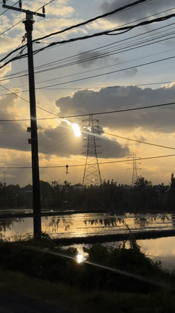 Overcast sunset glows through clouds above Mengwi power lines