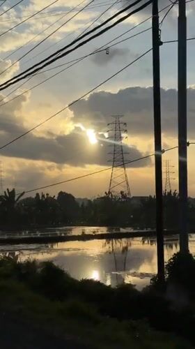 Overcast sunset glows through clouds above Mengwi power lines