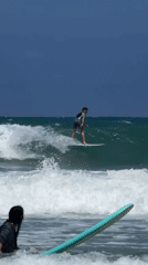 Surfer rides wave toward rocks near Tel Aviv navigation marker