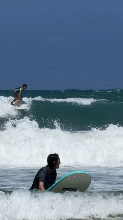 Surfer rides wave toward rocks near Tel Aviv navigation marker