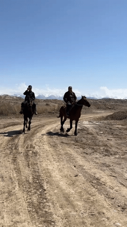 Two horsemen travel dirt path in rural Kyrgyzstan