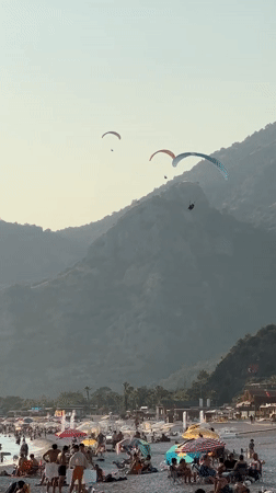 Paragliders soar over busy Fethiye beaches during sunny afternoon
