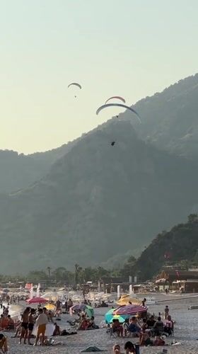 Paragliders soar over busy Fethiye beaches during sunny afternoon