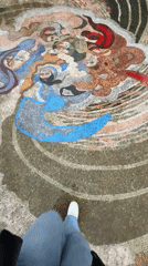 Person walks across mosaic near clock tower in Batumi