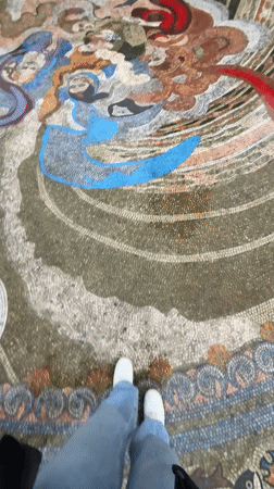 Person walks across mosaic near clock tower in Batumi