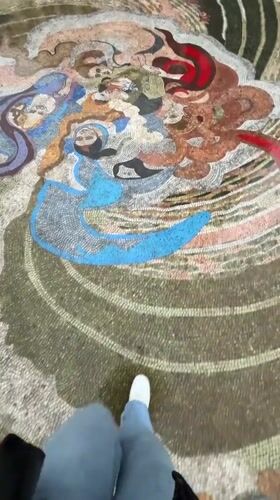 Person walks across mosaic near clock tower in Batumi