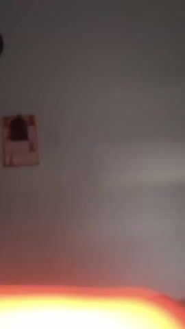 The video shows a close-up shot of a wall with a calendar hanging on it. The calendar appears to be old and worn, with faded colors and some damage. The top part of the calendar features an arch-shaped frame with a dark opening in the center, possibly a religious icon or a picture. Below this frame, the calendar pages display dates and some small images. The bottom part of the calendar is partially visible. The wall itself is a plain, light-colored surface. A faint red glow emanates from the bottom of the frame, suggesting an external light source or reflection.