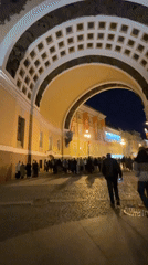 Pedestrians traverse illuminated archway in nighttime cobblestone square