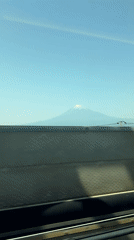 Train passenger films Mount Fuji through window on clear day