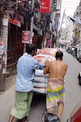 Workers push loaded handcart through narrow Dhaka street