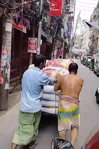 Workers push loaded handcart through narrow Dhaka street