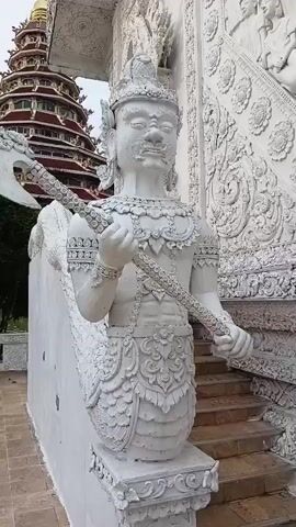 A close-up video of a white statue of a mythical creature holding an axe. The statue is detailed with intricate carvings. In the background, a large, multi-tiered pagoda with a golden spire is visible. The environment appears to be an outdoor temple or architectural site.