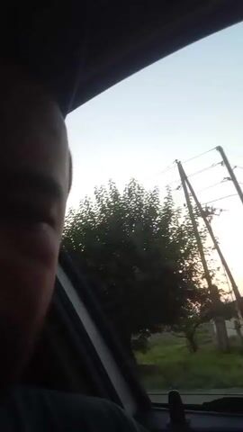 The video begins with a close-up of a person's face in silhouette, looking out a car window. The scene outside the window shows a sunset with trees and a telephone pole. The camera then pans to a closer shot of the person's face, who appears to be a man with a beard. The view outside the window changes to show a house and more trees. The video ends with another shot of the sunset through the car window.