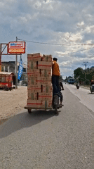 Two men transport stacked boxes via motorcycle in Indonesia