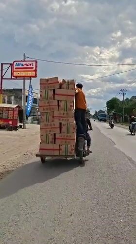 Two men transport stacked boxes via motorcycle in Indonesia