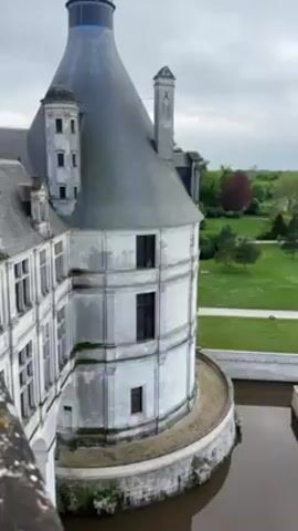 The camera is positioned outside what appears to be a castle, offering a view of the castle's architecture. The camera gradually zooms in on a window, revealing a statue positioned inside the room behind the window. The statue appears to be a bust of a person, likely a historical figure. The room is dimly lit, creating a shadowed effect that adds to the visual depth of the scene.