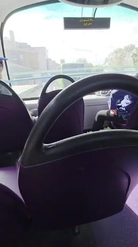 The video captures the interior of a public bus in Weston-super-Mare, United Kingdom. The camera is positioned to show the seating area, with purple seats and a speckled purple floor. Outside the windows, a bright, sunny day is visible with green trees and buildings suggesting an urban or suburban environment.

In the foreground, a person's legs and feet are visible, clad in black leggings and grey sneakers. The person appears to be seated on the bus. Further into the bus, another passenger is seen from behind, wearing a blue hoodie and dark pants. This passenger is seated in front of a window, looking outwards. The bus interior is clean and well-lit, with metal poles and handrails typical of public transport. The overall impression is of a routine bus journey on a pleasant day. There is no visible text within the frame.