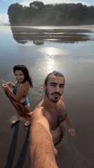Couple documents beach visit on black sand in Selemadeg