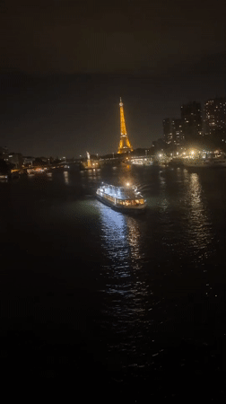 Eiffel Tower glows as a cruise boat crosses the Seine at night
