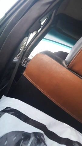 The video shows the interior of a car from the backseat. The front seat is upholstered in brown and black leather. There's a white plastic bag with a black design on the back seat. The car's interior is dark. The window is visible, showing a blurry view of the outside. The car seems to be moving.