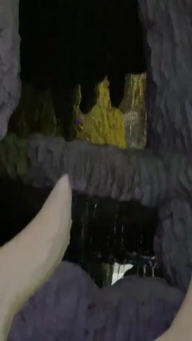 The video shows a dark cave-like environment with water dripping. There are illuminated rock formations and some areas are lit with yellow and green lights. A light blue light is also visible in one section. The camera pans through the cave, capturing the texture of the rocks and the water features.