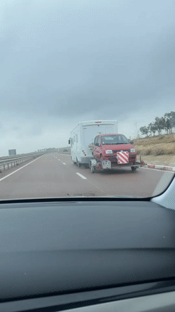Motorhome tows red car on trailer along Moroccan highway