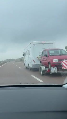 Motorhome tows red car on trailer along Moroccan highway