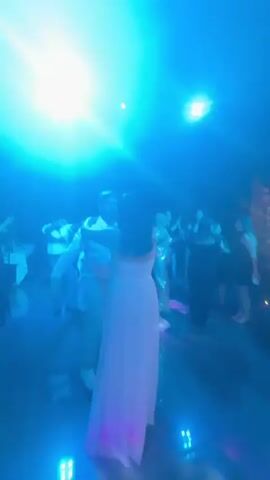 The video shows a wedding reception with people dancing. A woman in a white dress is dancing with a man in a light-colored shirt. The lighting changes between red and blue. There are other guests dancing in the background.