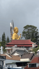 Golden Buddha statue overlooks red-roofed temple in Đà Lạt