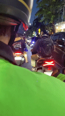 Motorcyclist in green jacket travels Kuta street at dusk