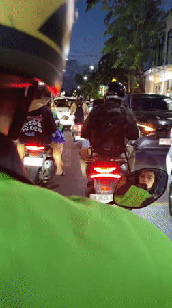 Motorcyclist in green jacket travels Kuta street at dusk