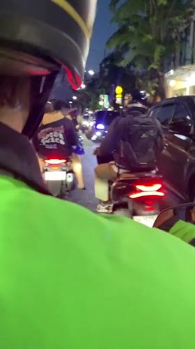 Motorcyclist in green jacket travels Kuta street at dusk