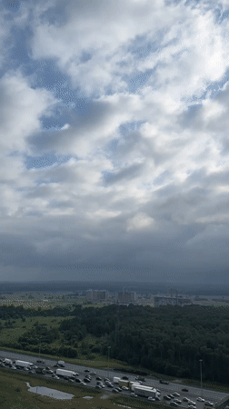 Highway traffic jam beside Kudrovo forest under breaking clouds