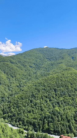Aerial view of forested Caucasus mountain with summit structure and valley river