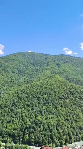 Aerial view of forested Caucasus mountain with summit structure and valley river