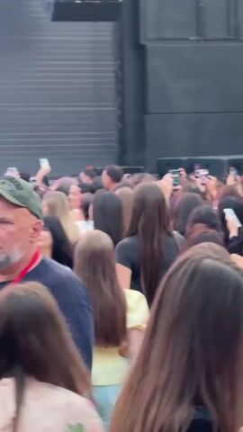 The video shows a crowd of people gathered in front of a stage. A large screen behind the stage displays the text "HAKAN ISIK SPECIAL INTERNATIONAL" in large, silver lettering with turquoise accents. Below the text, a man in a white shirt and sunglasses is visible behind a DJ booth. The crowd appears to be a mix of men and women, many of whom are holding up their phones, presumably to record or take pictures. The atmosphere seems to be that of a concert or event. The camera movement is slightly shaky, suggesting it was filmed by someone in the audience.