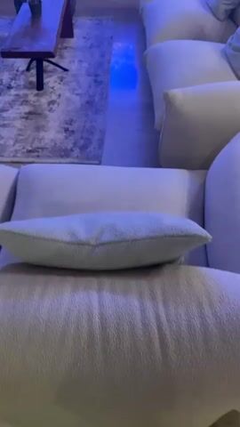 This video shows a living room area with multiple sofas, a coffee table, a rug, and a large screen displaying an underwater scene with many fish. The room is lit with blue ambient lighting, and the overall atmosphere is dark and moody. The camera pans across the room, focusing on the different elements of the space. There are no people visible in the video.